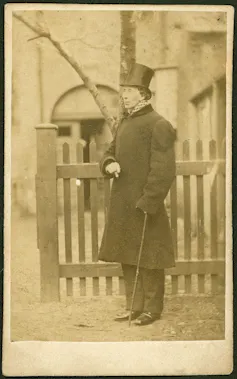 Fotografía virada a sepia de un hombre con abrigo, chistera y bastón.