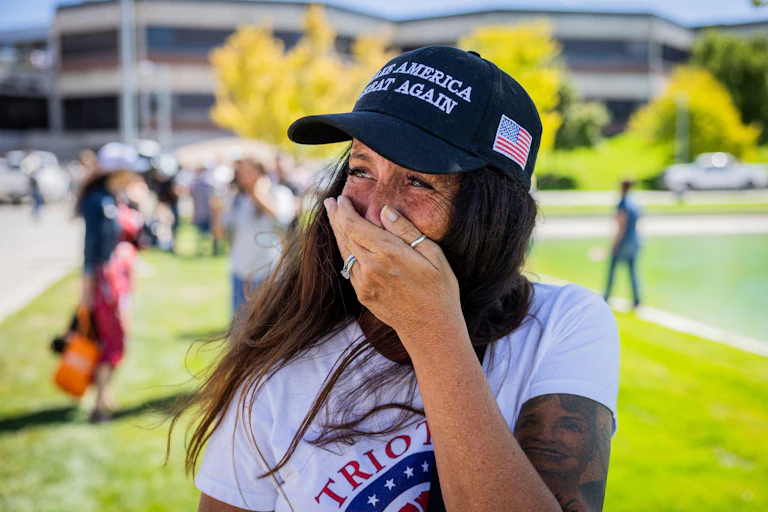 A young woman wearing a blue Maga hat holds her hand over her mouth as she cries.