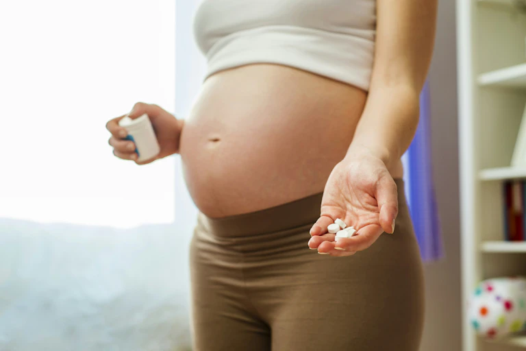 Cropped photo of a pregnant woman holding a medication bottle in one hand and tablets in the other