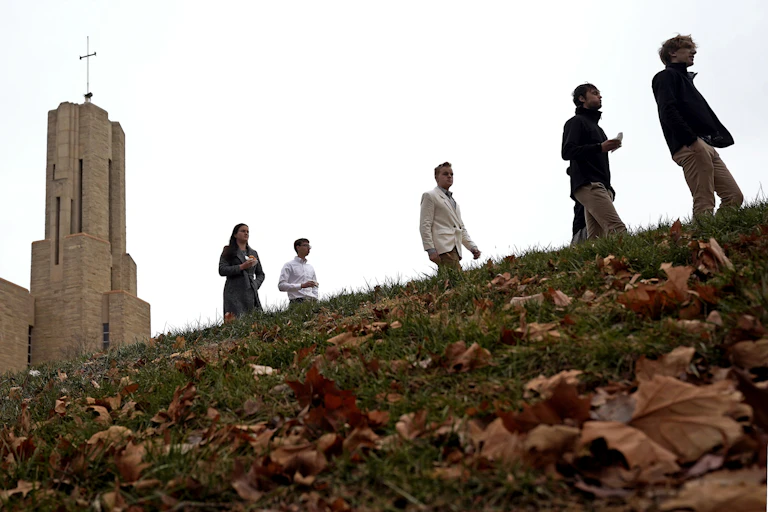 Five young adults walk along a hill in front of a large church with a cross on top.