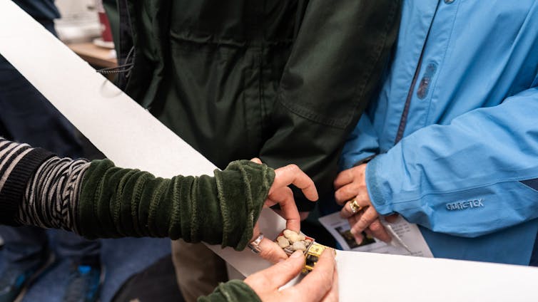A close up of people's hands with a small toy lorry in the middle.