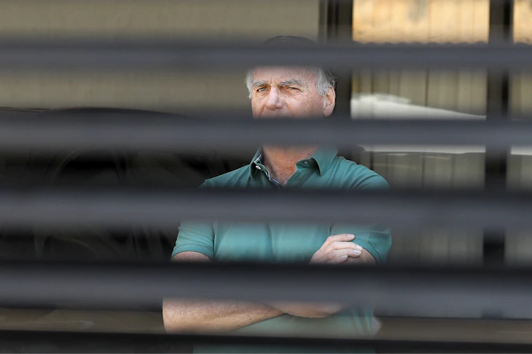 A man with folded arms is seen behind blinds