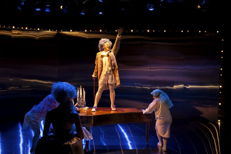 An actor stands on a piano.