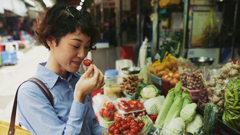A woman smells a tomato at an outdoor food market.