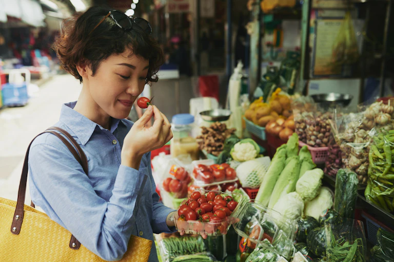 A woman smells a tomato at an outdoor food market.