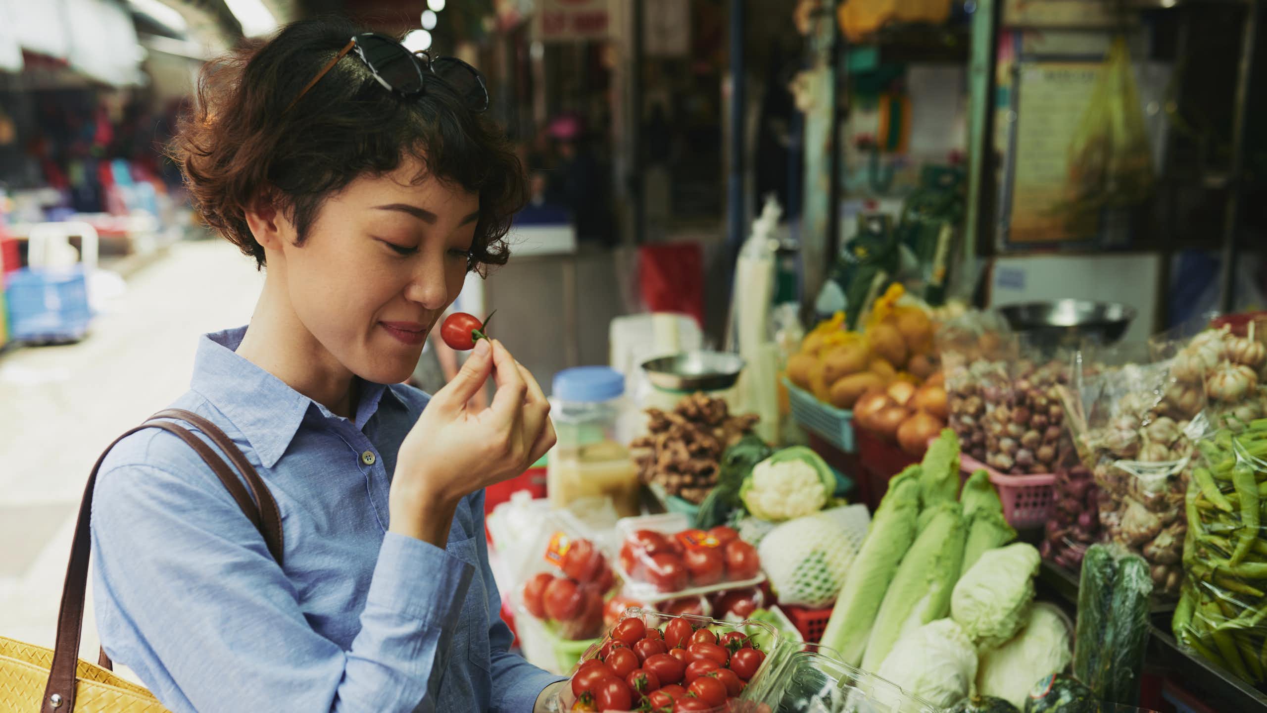 A woman smells a tomato at an outdoor food market.