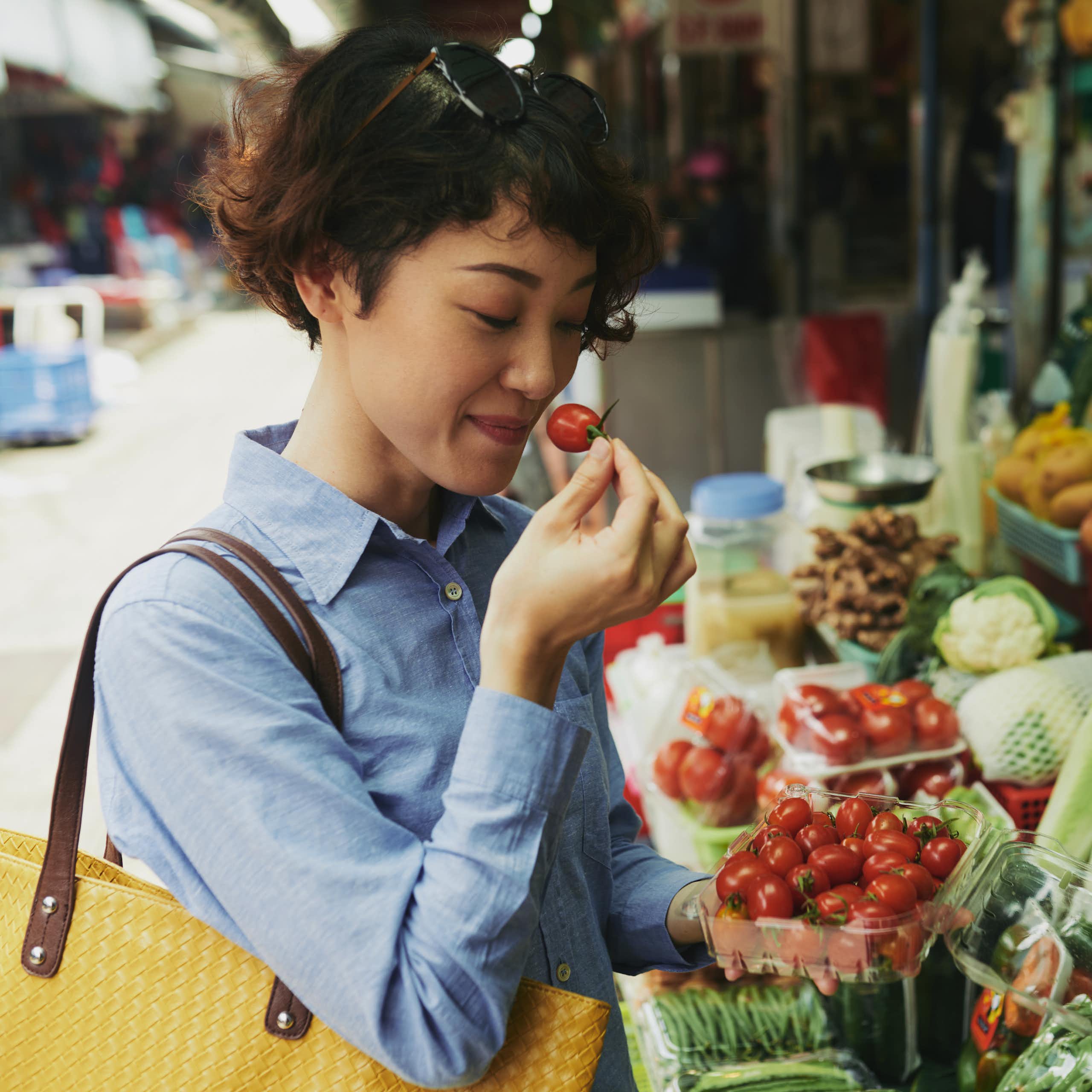 A woman smells a tomato at an outdoor food market.