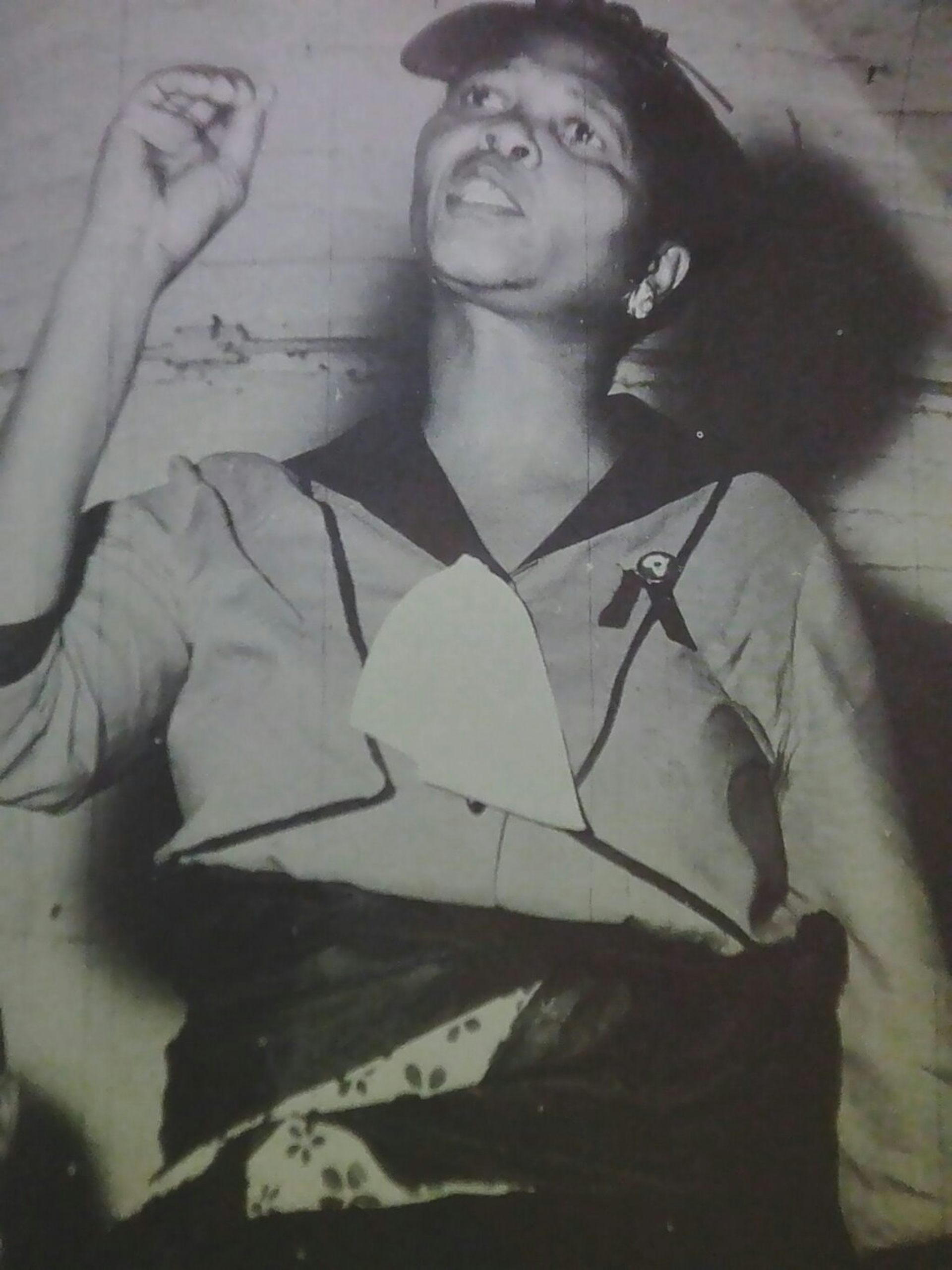 A black and white photo of an African woman speaking, her hand in the air to emphasise a point.