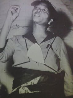 A black and white photo of an African woman speaking, her hand in the air to emphasise a point.