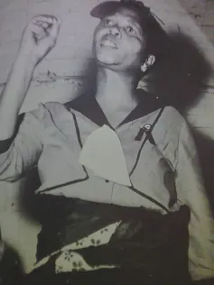 A black and white photo of an African woman speaking, her hand in the air to emphasise a point.
