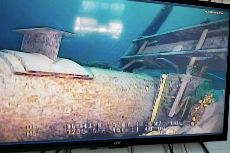 A large pipe running underwater is seen illuminated by artificial lights.