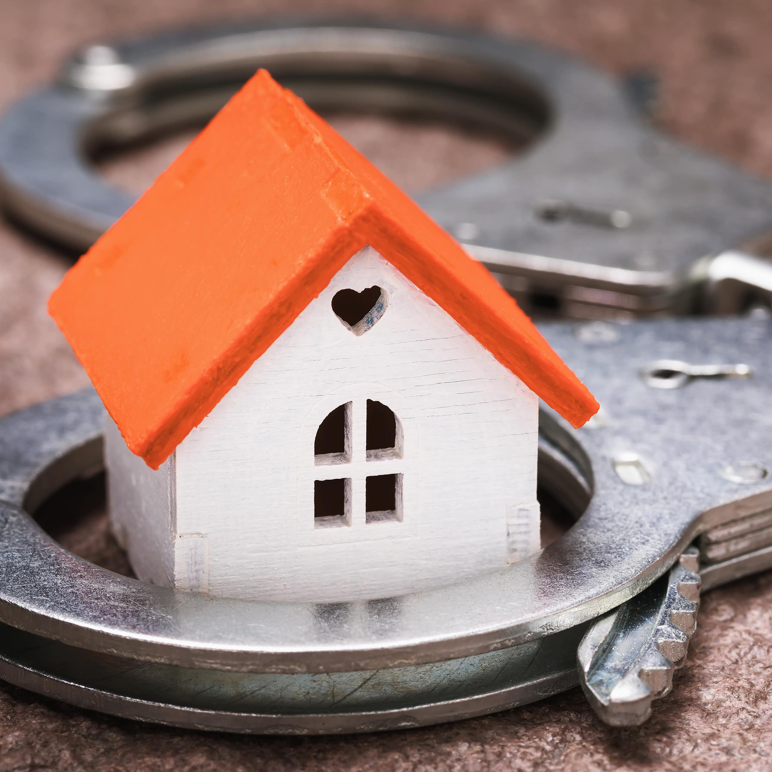 A small toy house is juxtaposed with a pair of handcuffs.