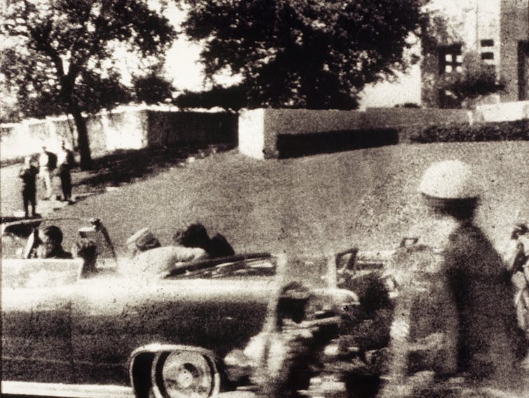 A fuzzy photo of a large car with a woman leaning over in the back seat to help a slumped man next to her.