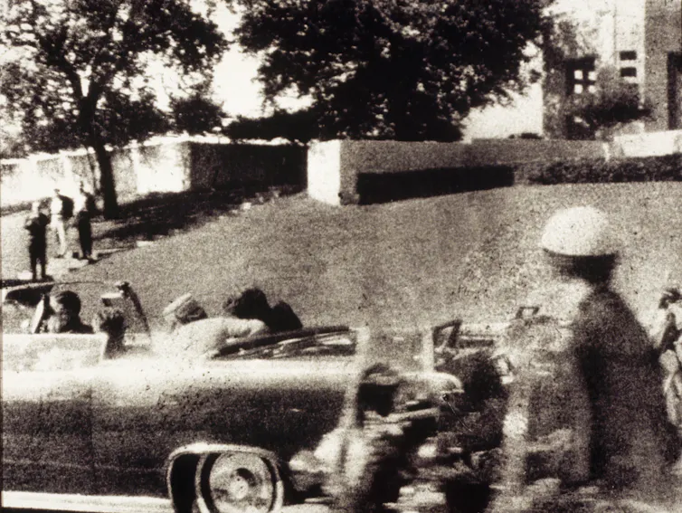 A fuzzy photo of a large car with a woman leaning over in the back seat to help a slumped man next to her.