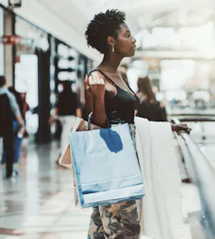 A woman is in a mall shopping with two shopping bags hanging off her arm.