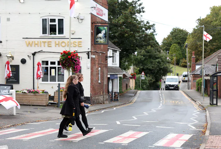 Two people walking on a zebra crossing painted to look like St George's flags.