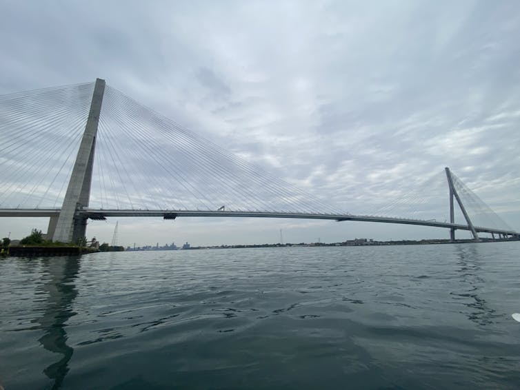 El gran puente de cable cruza sobre un gran cuerpo de agua. Las nubes oscuras con puntos aparecen en el fondo.