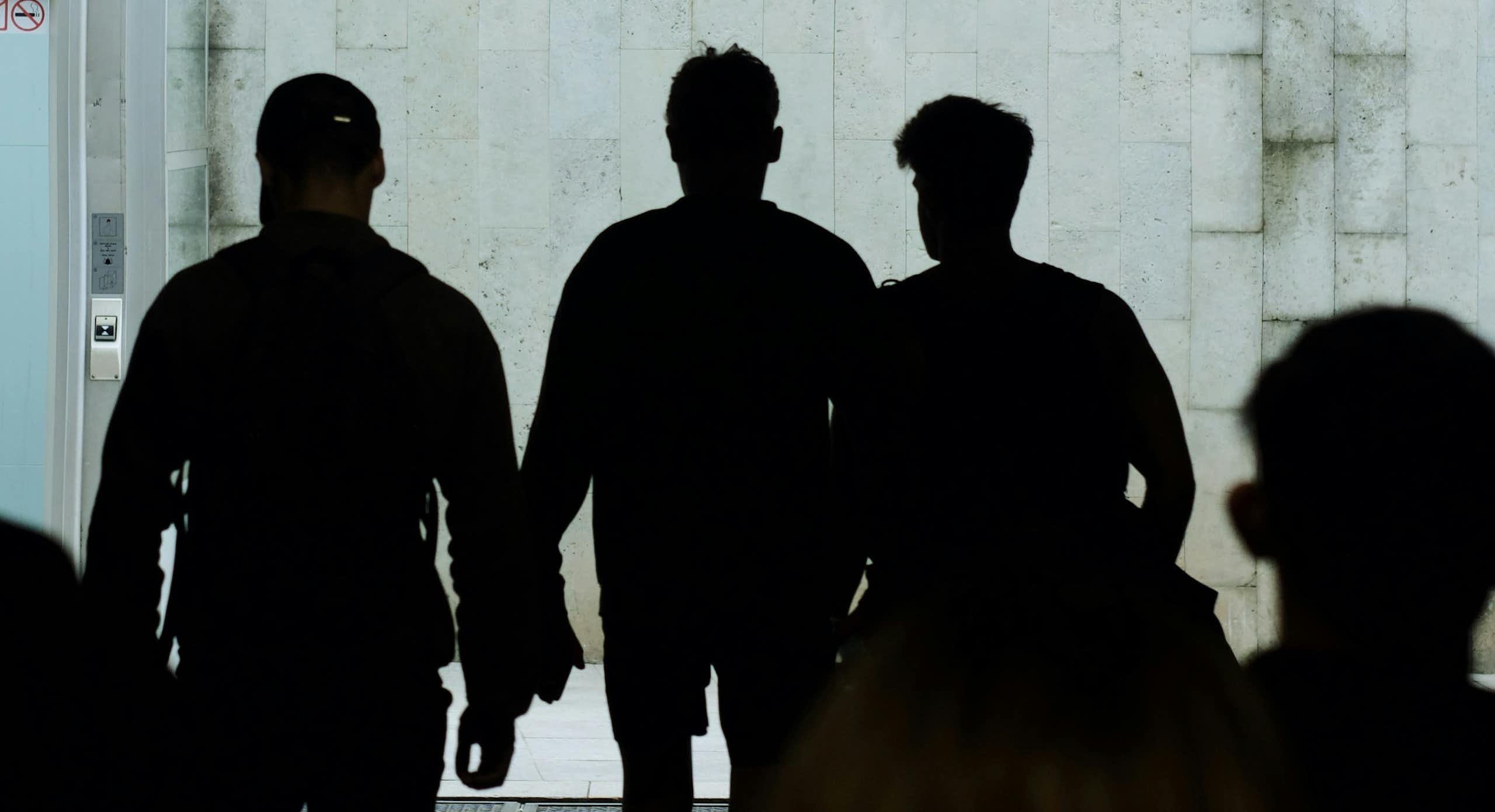 Silhouettes of young people are seen on a public street at night.