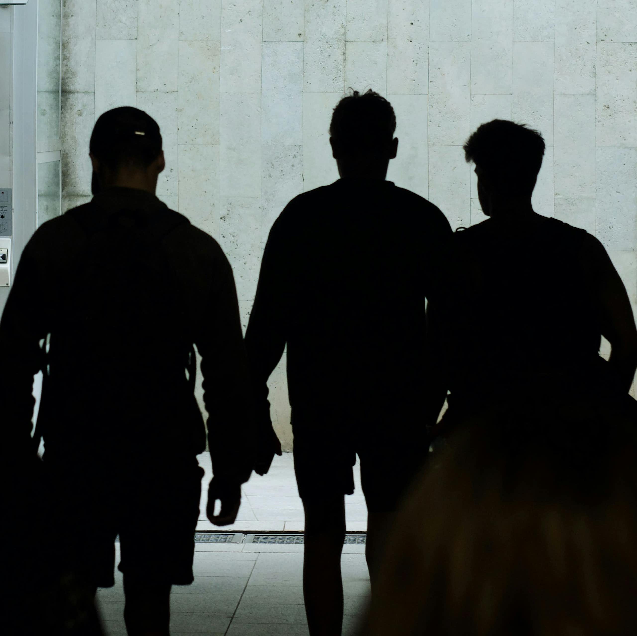 Silhouettes of young people are seen on a public street at night.