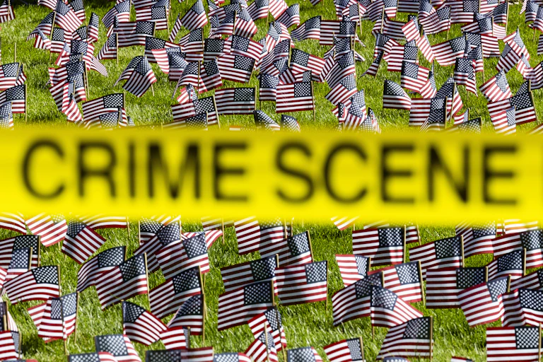 Rows of small American flags with yellow tape reading CRIME SCENE in the foreground.