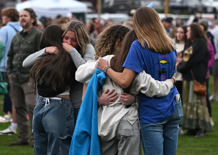 High school age children embrace in the foreground, with other bystanders in the background.