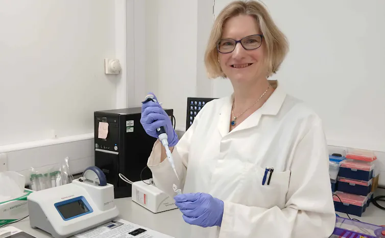 Katherine Steele wearing a white lab coat in a laboratory with scientific instruments.