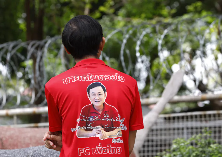 A man in a red t-shirt depicting Thaksin Shinawatra's face stands outside a prison.