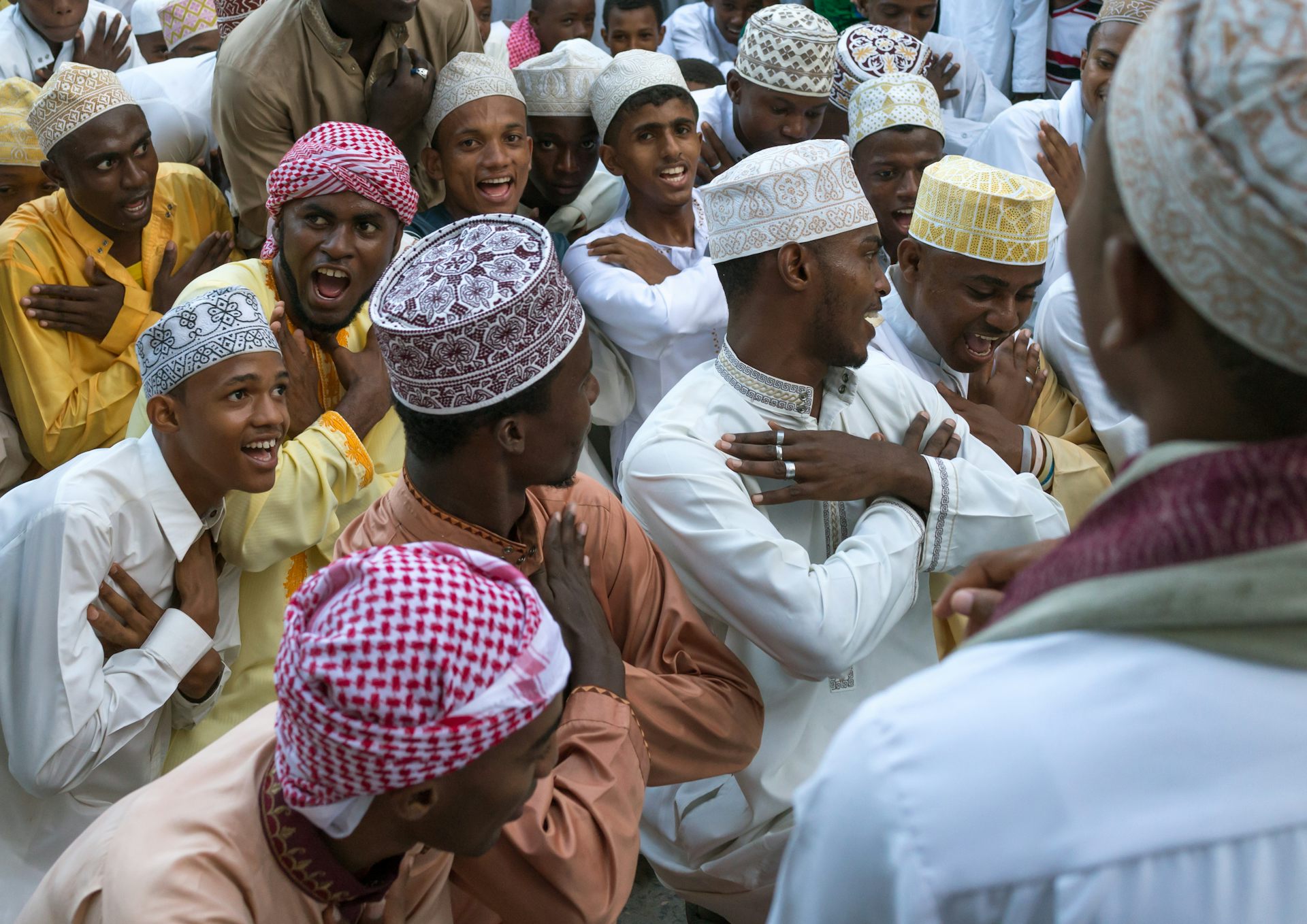 A group of young men in Muslim attire laugh and smile and cross their arms over their chests as they move.