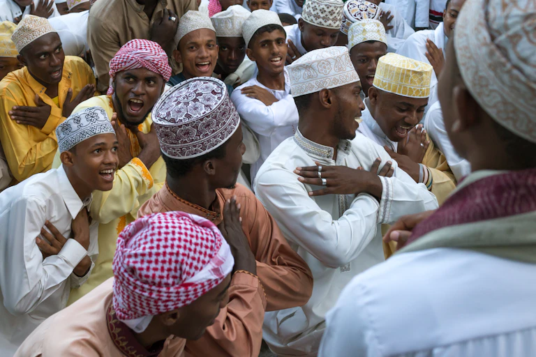 A group of young men in Muslim attire laugh and smile and cross their arms over their chests as they move.
