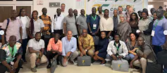 A group of about 30 people pose for a photo at a conference