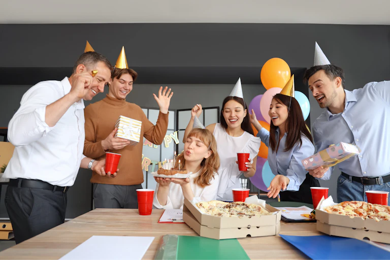 des gens au bureau qui font une fête d'anniversaire avec des chapeaux pointus en carton sur la tête