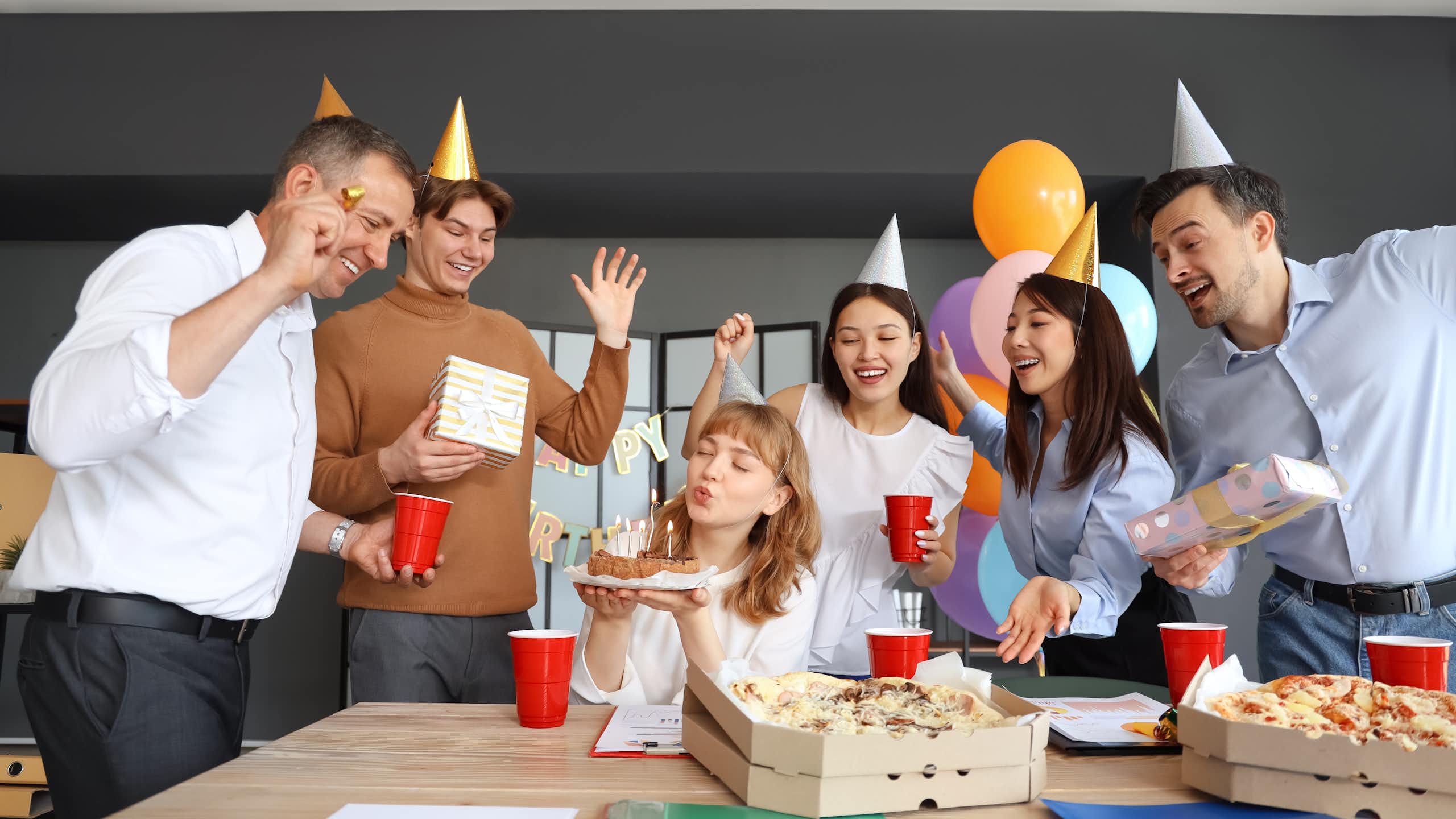 des gens au bureau qui font une fête d'anniversaire avec des chapeaux pointus en carton sur la tête