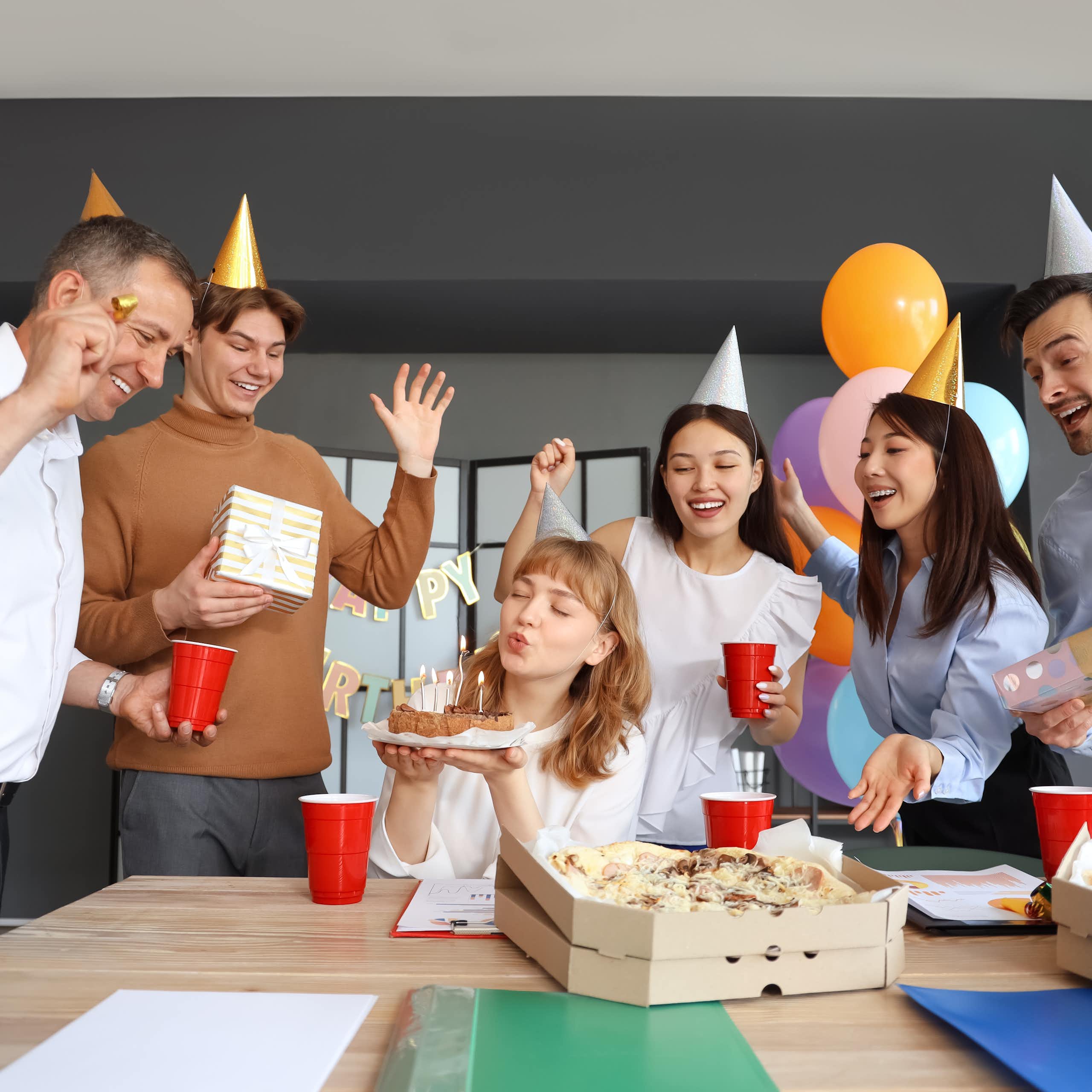 des gens au bureau qui font une fête d'anniversaire avec des chapeaux pointus en carton sur la tête