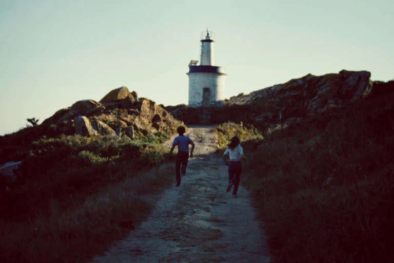 Un chico y una chica corren hacia un faro.