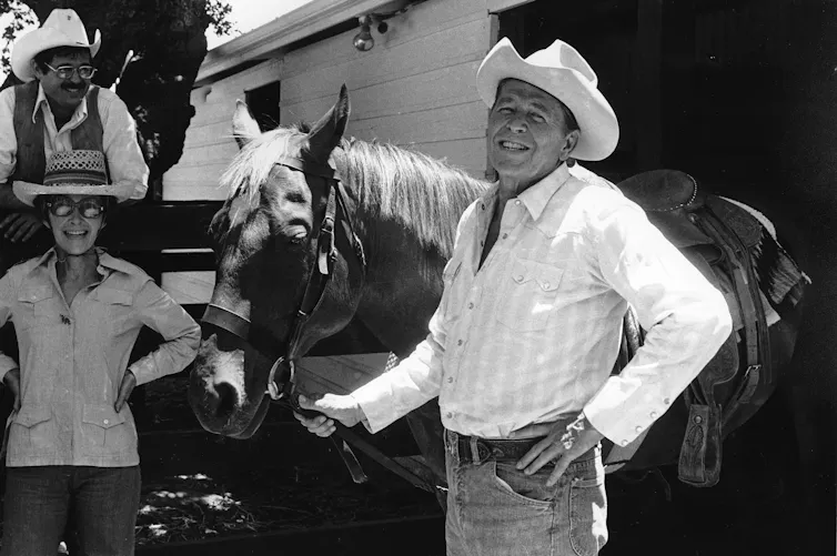 A man in a cowboy hat holding the reins of a horse.