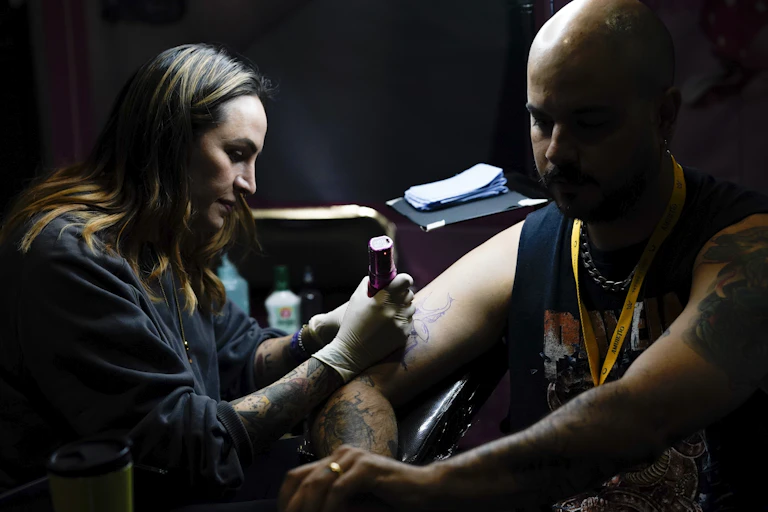 A woman tattoos a man's upper arm
