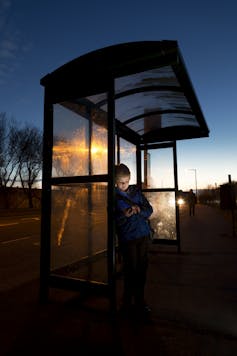 young schoolboy using smartphone while waiting for the bus.