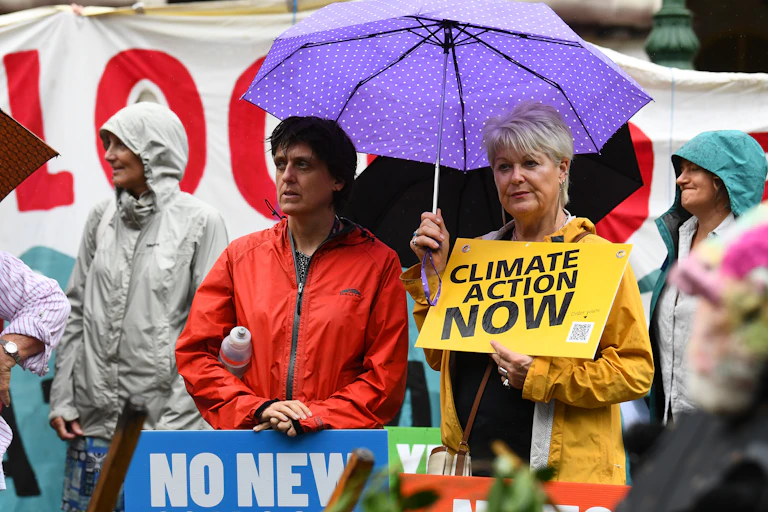Two people stand under umbrella holding a sign that says 'climate action now'