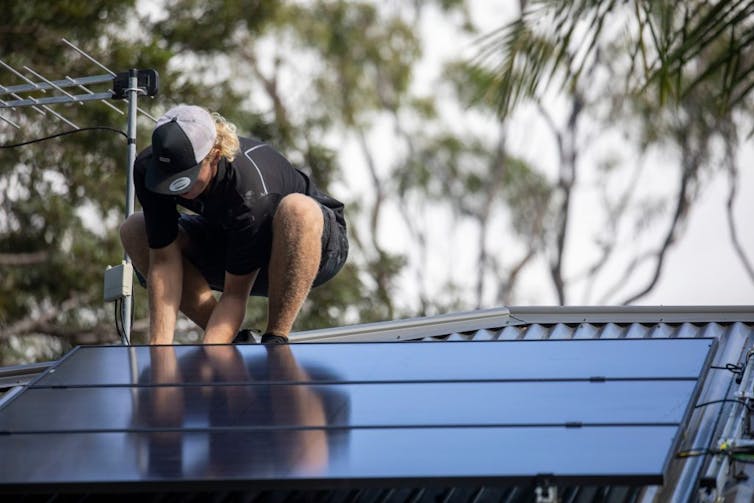 A man installs solar panels on a roof.