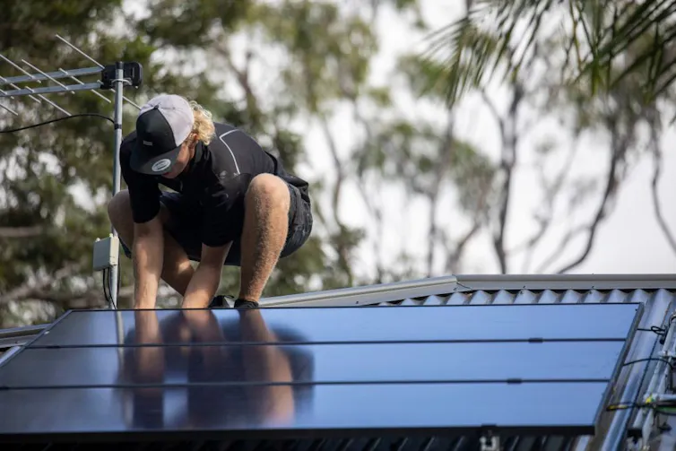 A man installs solar panels on a roof.