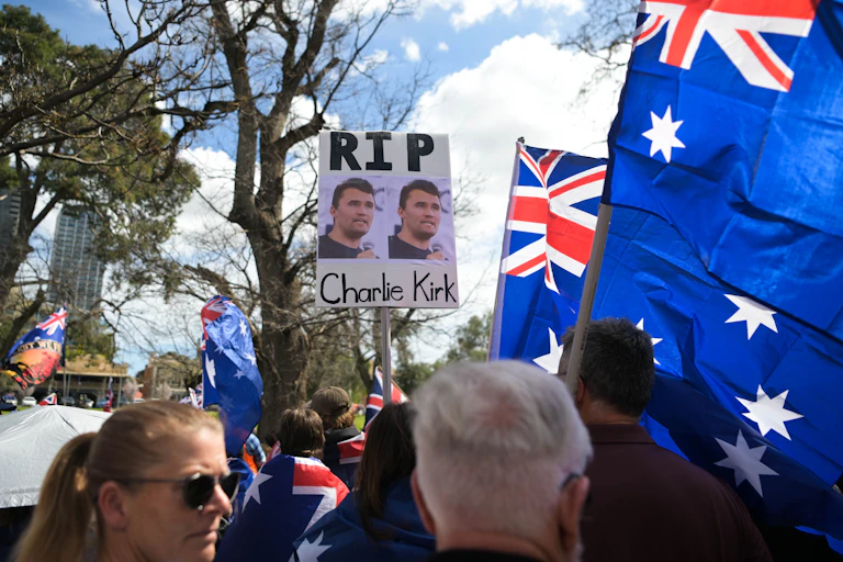 A sign held up at a protest saying RIP Charlie Kirk, with Australian flags around it.