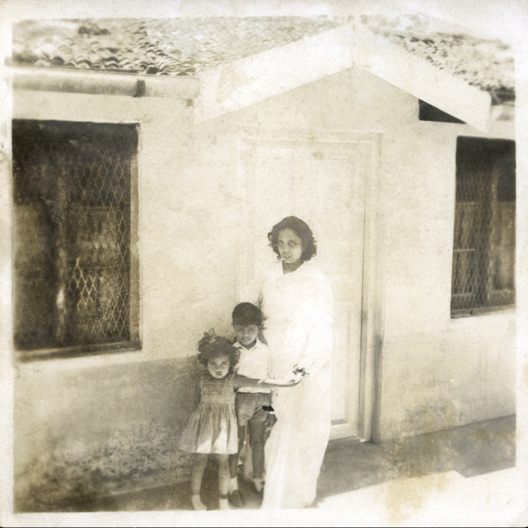 Two glum-looking children stand close to their mother.