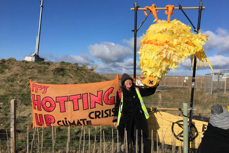 Woman standing by orange and red protest banner 'it's hotting up'