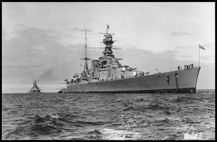 A black-and-white photo shows to large battle cruisers at anchor in a harbour.