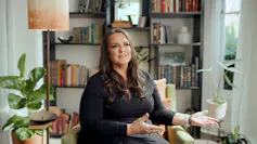 A woman sitting on a couch is talking and moving her hands in the air.