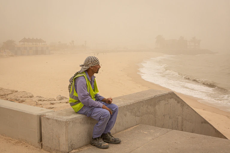 A worker looking out to sea in the middle of a sandstorm.