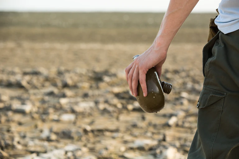 A man holds a water container in a desert.