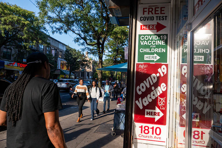Street view of person walking past glass doors of a shop, with signs on the sign reading 'COVID-19 VACCINE FOR CHILDREN HERE'