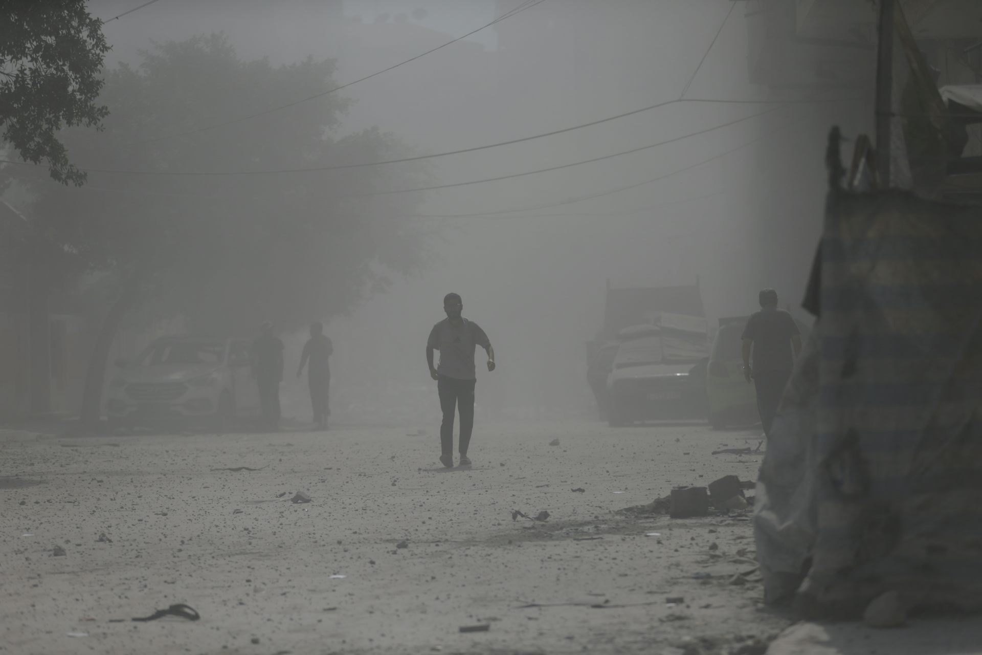 People walk though a dusty street of rubble.