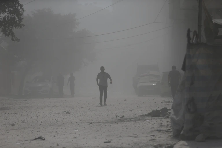 People walk though a dusty street of rubble.